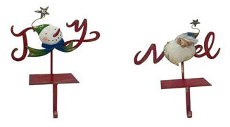 Two red metal Christmas stocking holders with decorative elements including the letters 'Joy' and 'Noel', a snowman, and Santa.