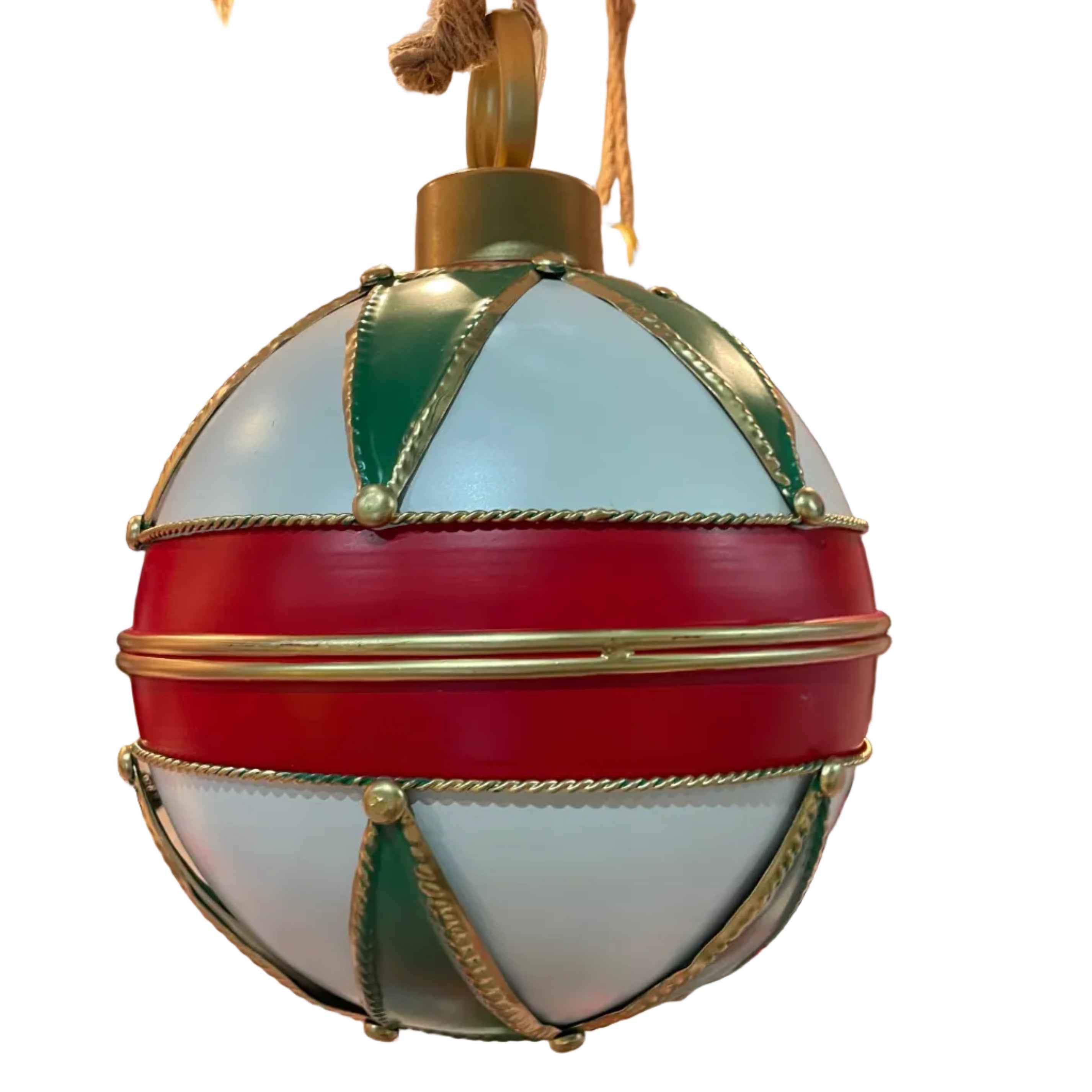 A large metal Christmas ornament hanging, featuring a white body with bold red horizontal bands, green geometric panels, and gold rope trim details.