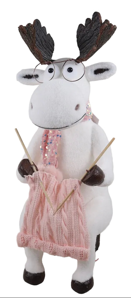 A white elk wearing glasses and a pink sparkling scarf, knitting a sweater, seated on a log base.