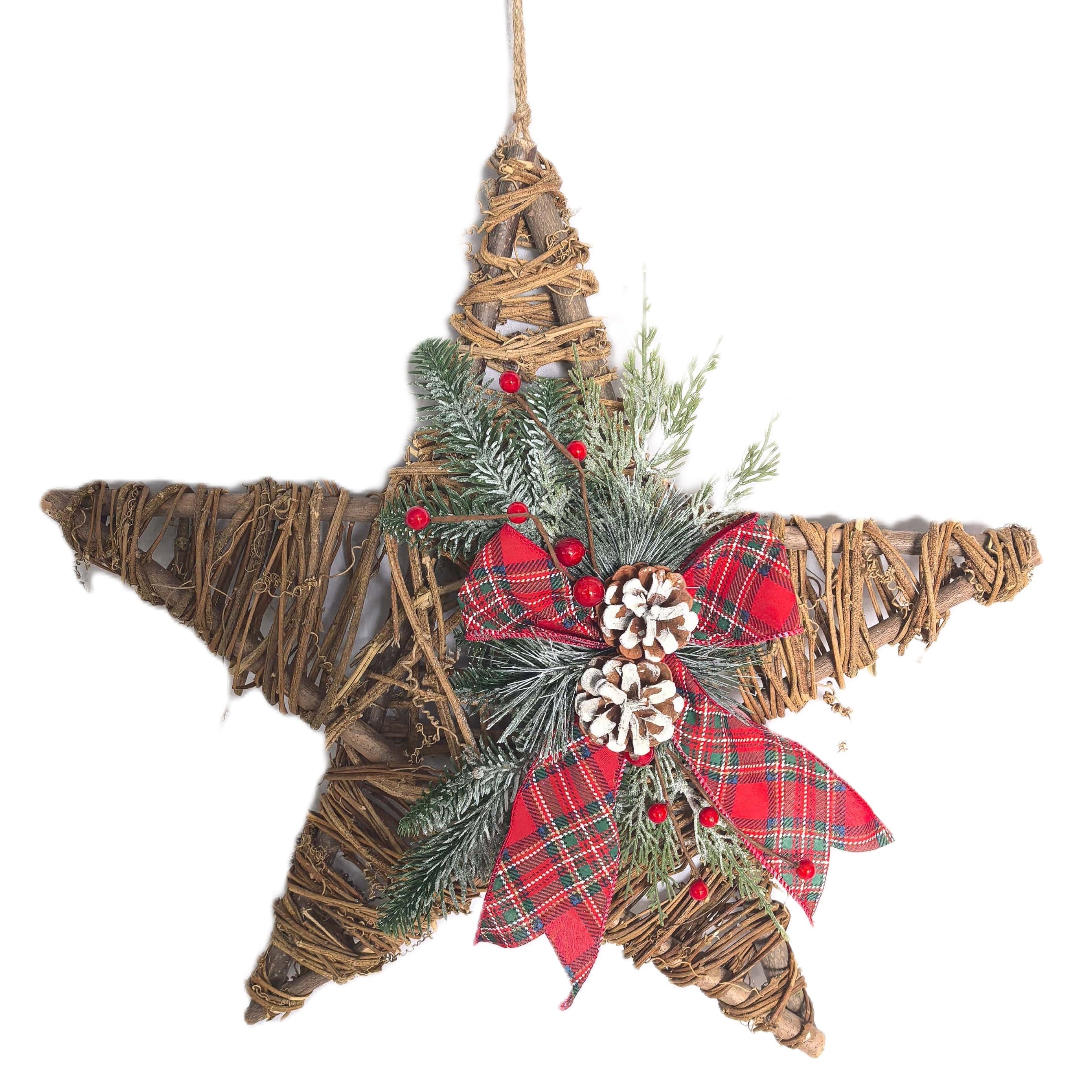 A rustic five-point star Christmas hanging decoration made from natural twigs, decorated with a red plaid ribbon bow, green pine branches, small pinecones, and red berries, suspended by a twine string.