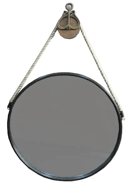 A circular wall mirror and a black frame, suspended by a thick white rope from a bronze pulley system