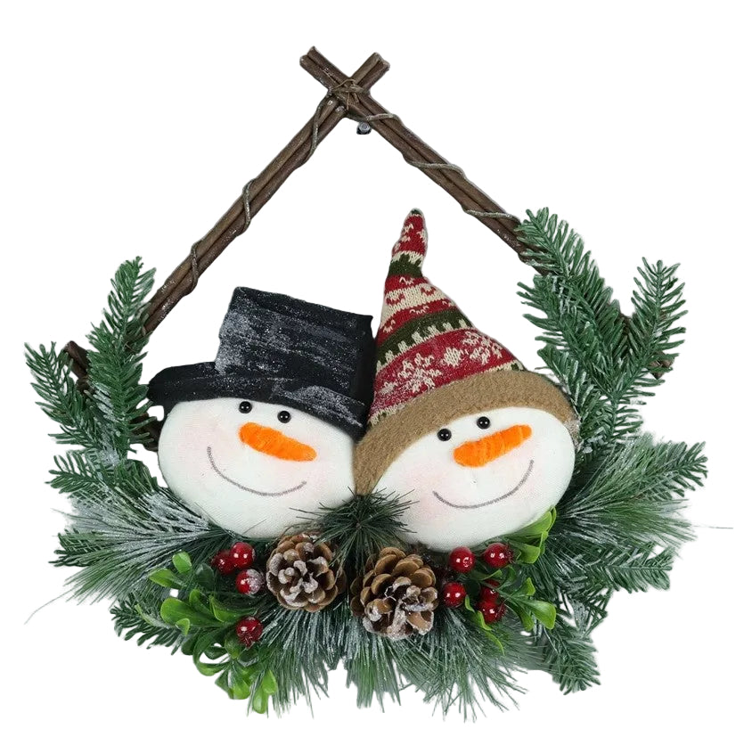 A holiday decoration featuring two plush snowmen with ornamental hats, surrounded by green artificial foliage and red and white Christmas ornaments, against a plain background.