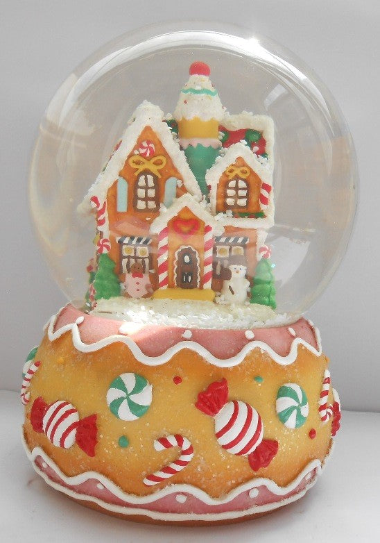 A decorative gingerbread house water globe with a clear sphere on top showcasing a small house with multicolored details, sitting on a base decorated with candy cane and gingerbread designs.