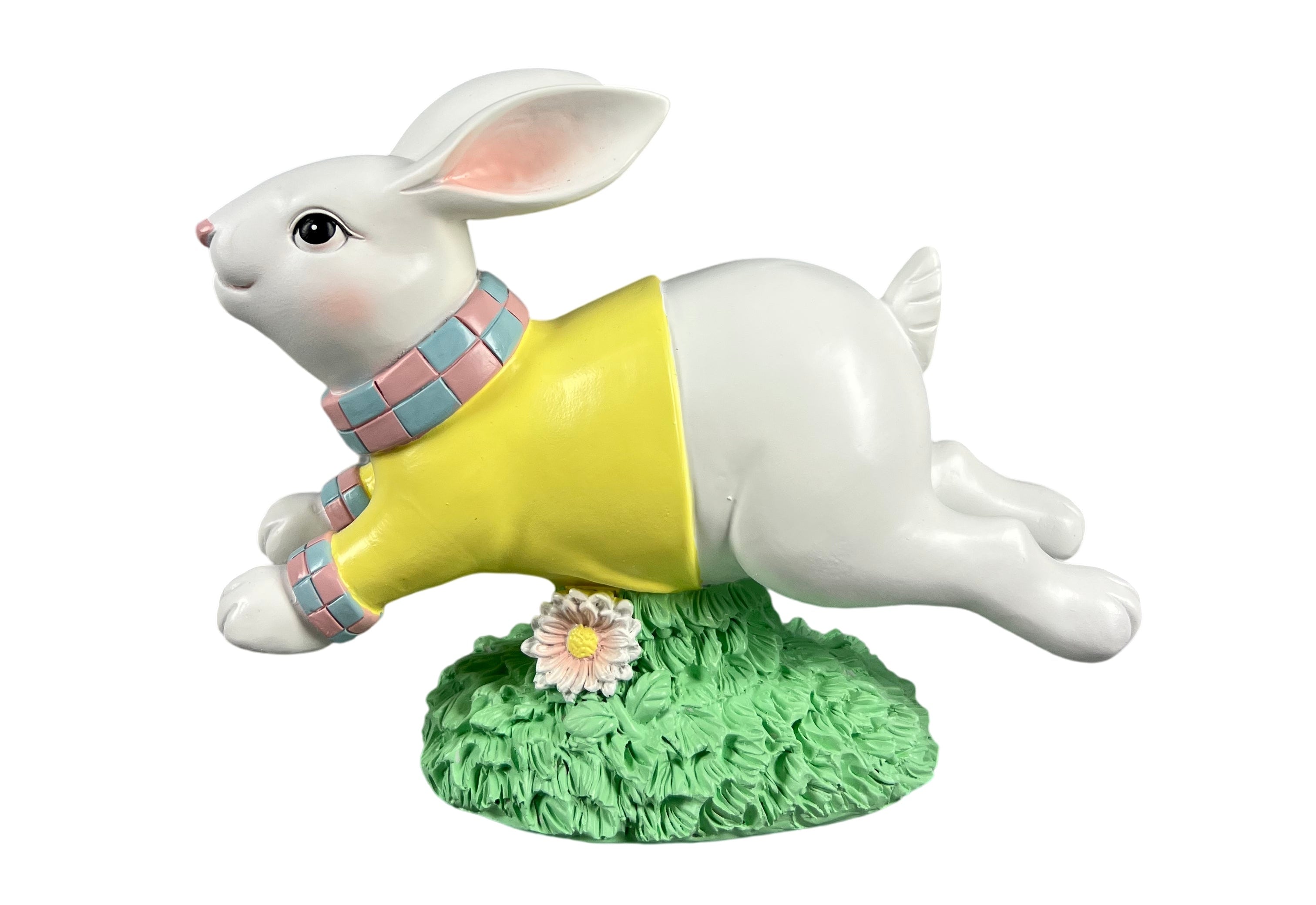 A white rabbit figurine wearing a yellow sweater and a blue-and-pink plaid scarf, standing on a green grassy base with a small white flower.