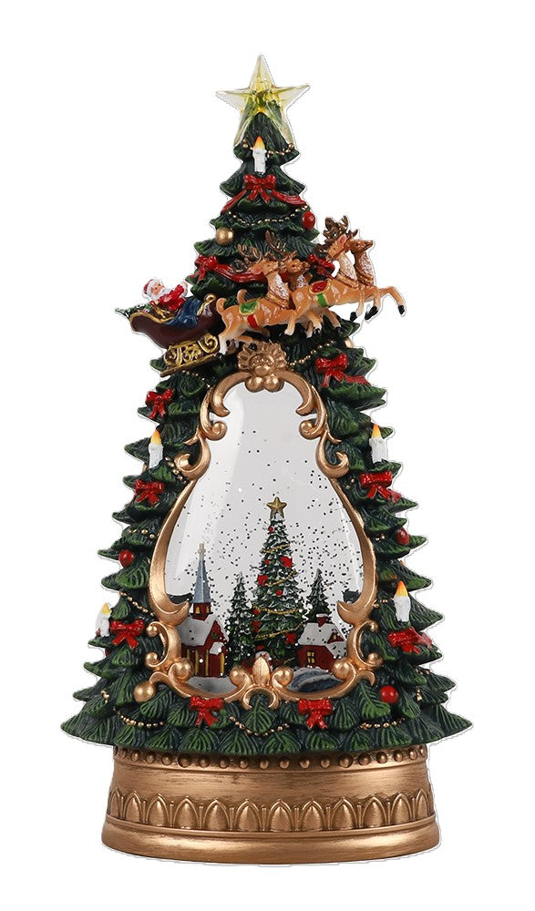 A decorative musical tabletop Christmas tree glitter water snow globe, a star topper, reindeer and sleigh detail, and a snowy village scene visible through the centre. The base is gold-toned and the tree is primarily green with red and gold accents. 
