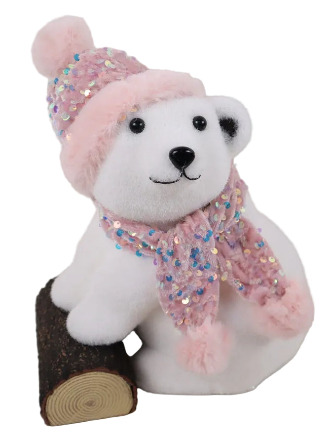 A  white bear wearing a pink hat and scarf, sitting next to a brown log.