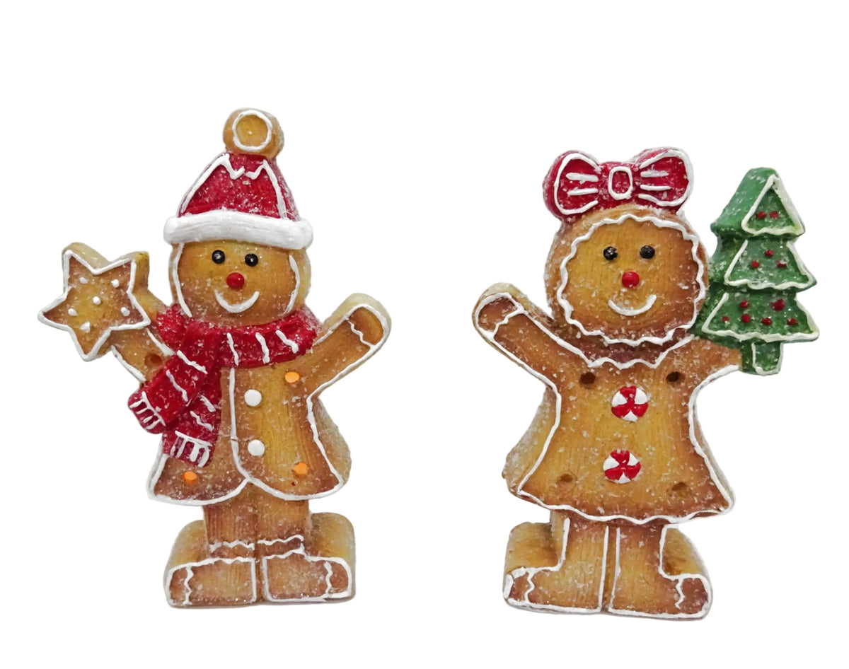 Two decorative gingerbread figurines representing a boy and a girl, with the boy wearing a Santa hat and the girl a Christmas bow.