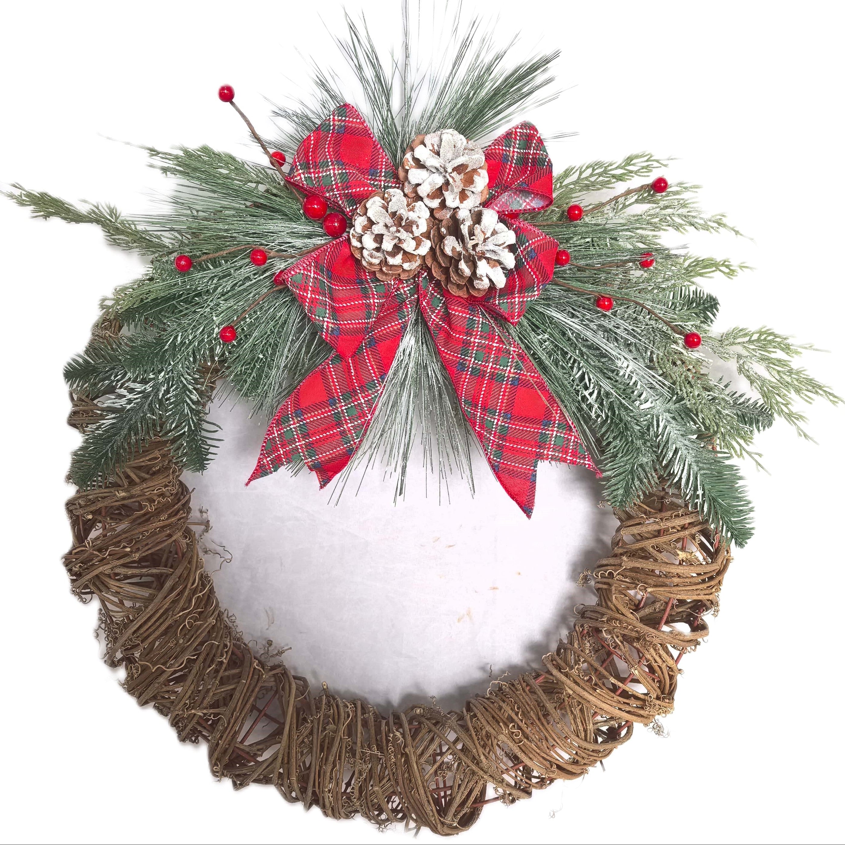A round Christmas wreath with a natural brown woven base, a white faux-snow center, green pine branches around the edge, small red berries, and a red plaid bow with a white pinecone at the top.